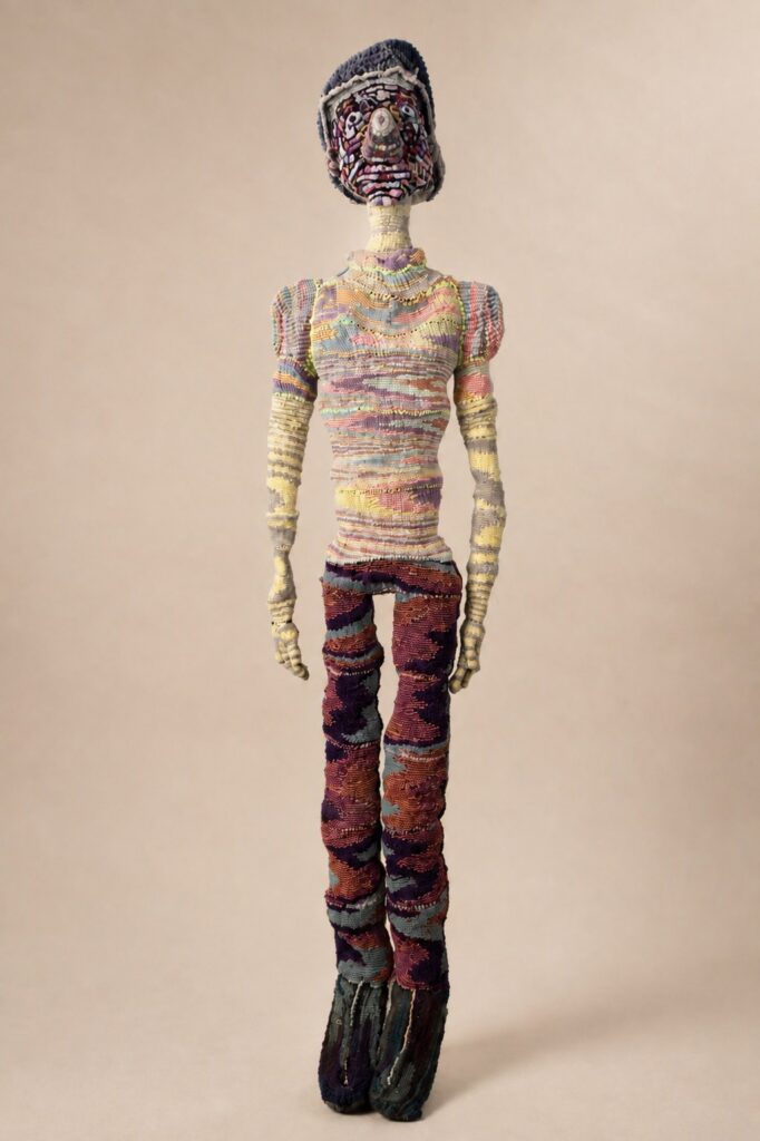 Standing life-size figure in a striped sweater and plum trousers. Pipe cleaner sculpture by Ted Fullwood